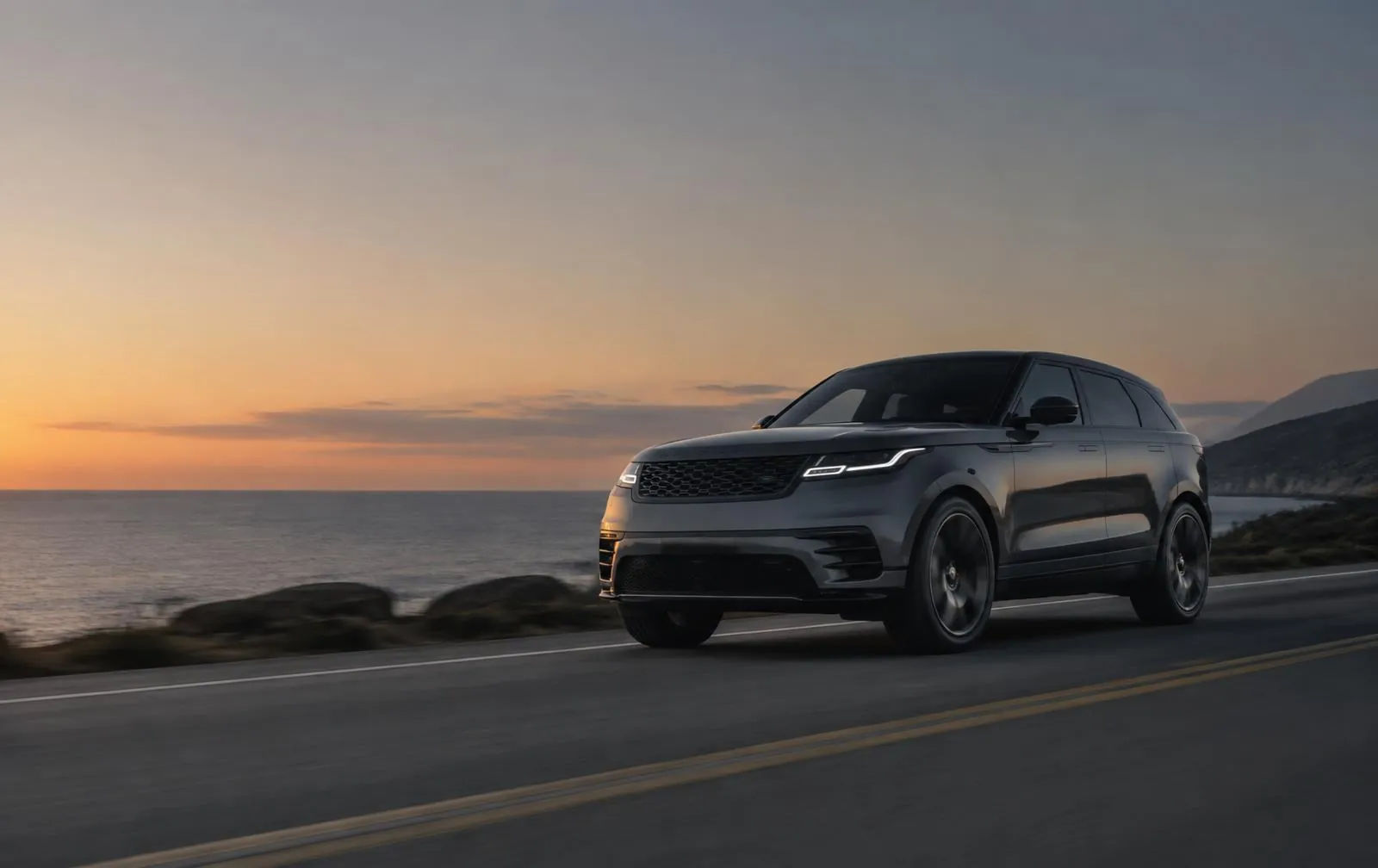 Dark grey SUV driving along a coastal road at dusk